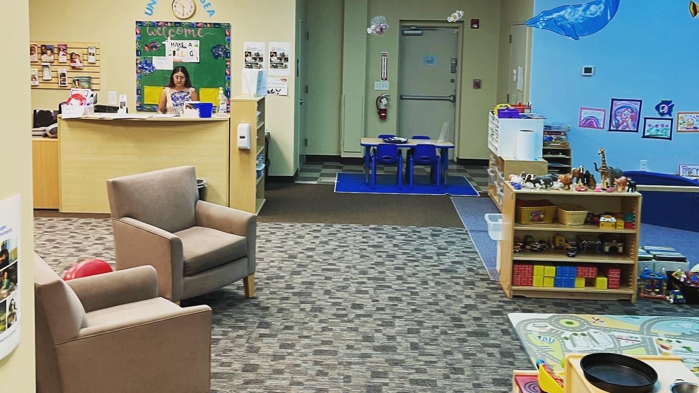 Interior of a children's play area featuring a reception desk, seating, and various toys and educational materials for young children.