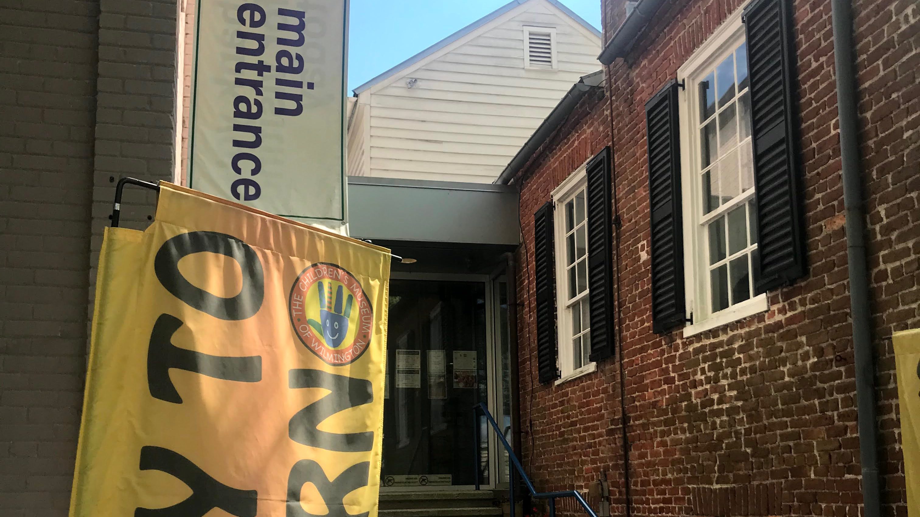 Main entrance of the Children's Museum of Wilmington, featuring a sign and colorful banner.
