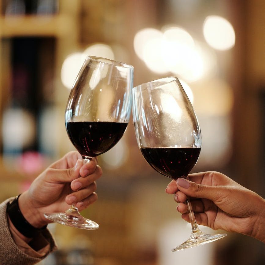 hands toasting wine glasses with red wine
