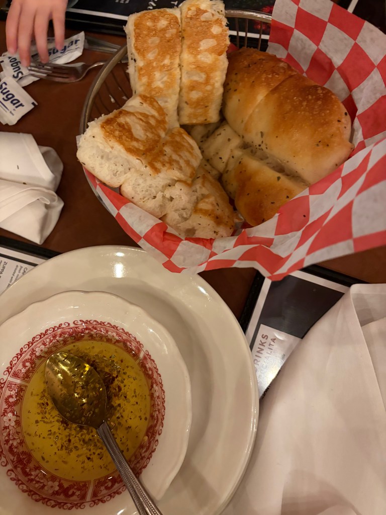 A basket of assorted breadsticks and biscuits served with a small dish of olive oil and herbs.