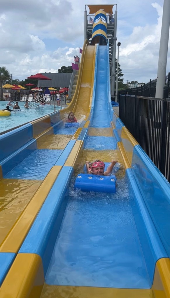 A child enjoying a water slide at a waterpark, splashing into the pool below with a bright blue float and wearing pink goggles.