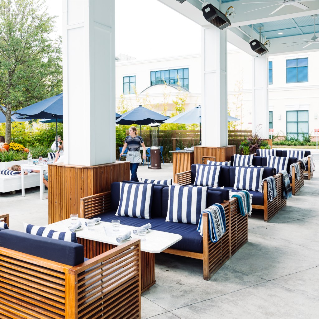 Outdoor patio seating area at Perla Raw Bar featuring striped couches, tables, and umbrellas.