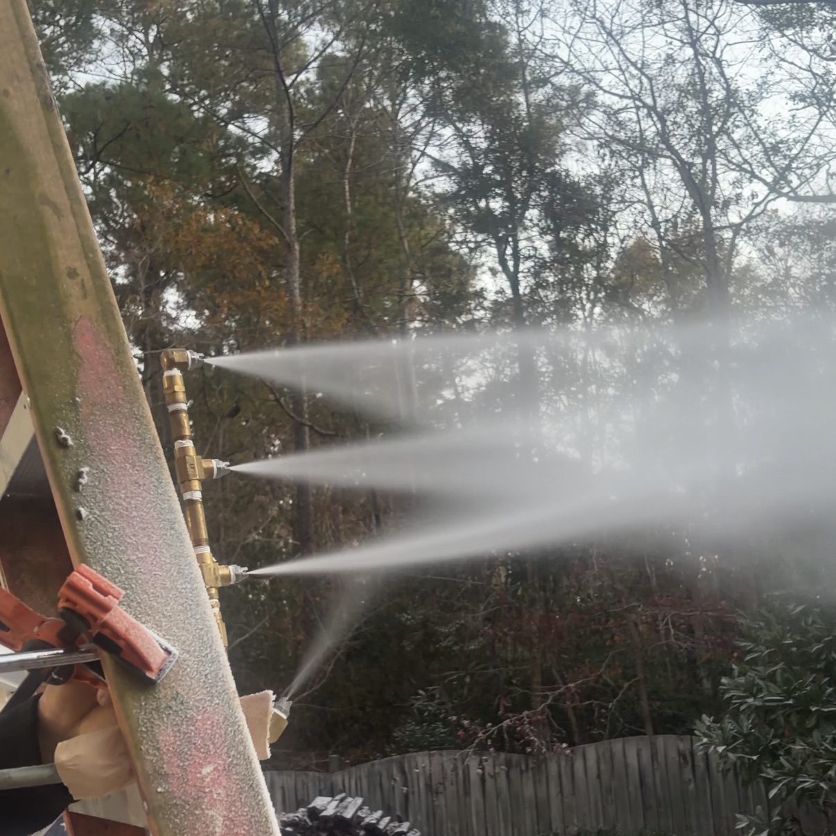 A backyard snow machine spraying artificial snow, with trees in the background and a partially snow-covered ground.