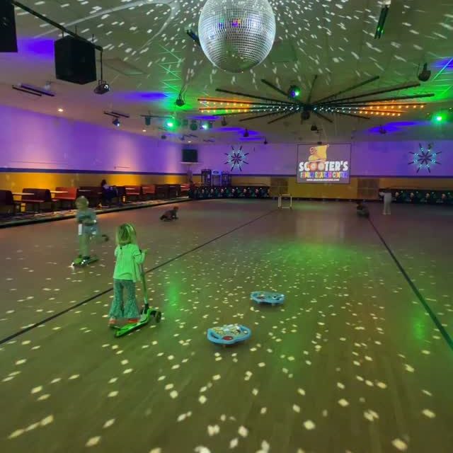 Kids playing on scooters in a roller rink with a disco ball and colorful lights.